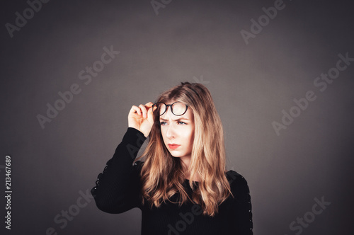 Junge Frau sieht skeptisch unter Brille durch in die Ferne