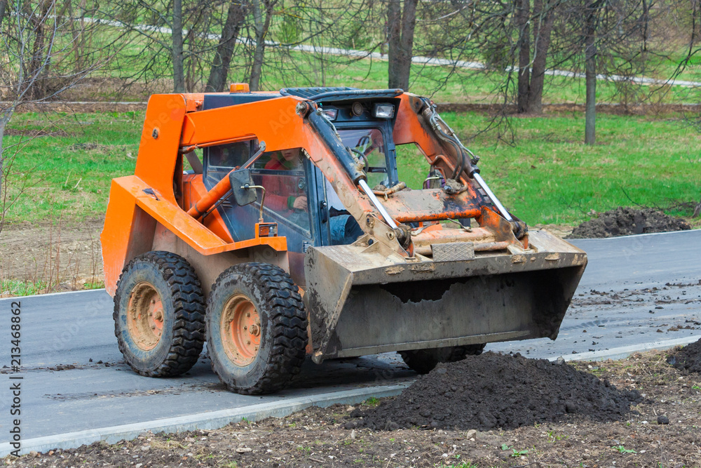 Orange bulldozer unloads black soil. Works on the development of the park area.