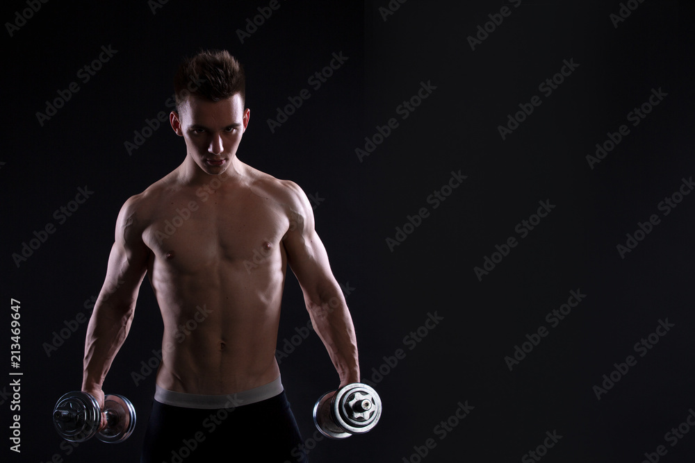 Athletic young man with a dumbbell on a black background. Naked torso, muscular body. Strong chest and shoulder muscles. Studio shot, low key. Bodybuilding concept Athletic young man with a dumbbell on a black background. Naked torso, muscular body. Strong chest and shoulder muscles. Studio shot, low key. Bodybuilding concept