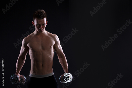 Athletic young man with a dumbbell on a black background. Naked torso, muscular body. Strong chest and shoulder muscles. Studio shot, low key. Bodybuilding concept