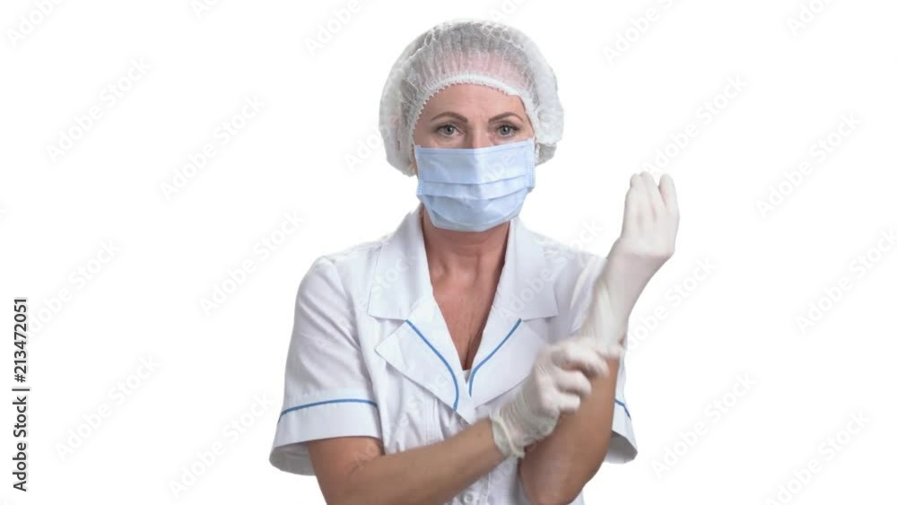 Female surgeon putting on a glove. Female medicine doctor in protective mask and cap putting on white protective glove, white isolated background. Female surgeon putting on a glove. Female medicine doctor in protective mask and cap putting on white protective glove, white isolated background.