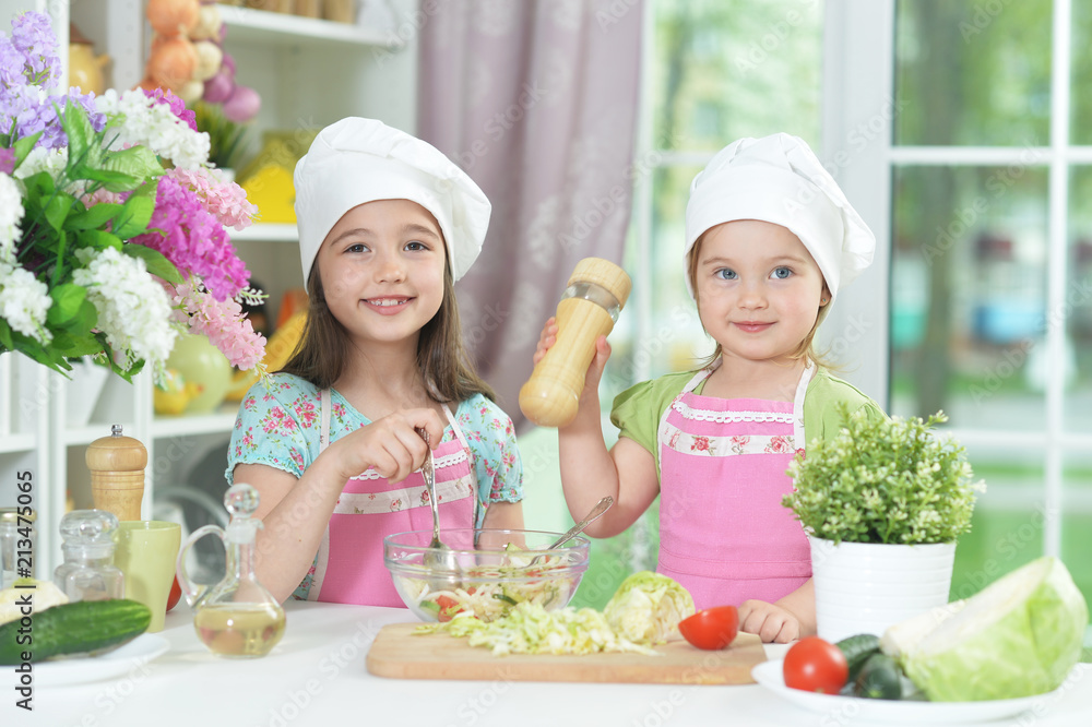 Two adorable little girls in aprons preparing delicious salad Two adorable little girls in aprons preparing delicious salad