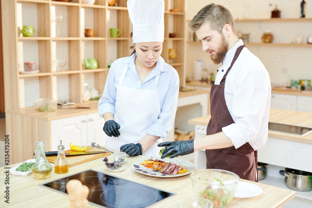 Waist up portrait of two professional chefs cooking delicious dishes in modern kitchen standing at wooden table , copy space