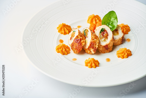 Poultry rolls with carrot puree, orange on a white plate
