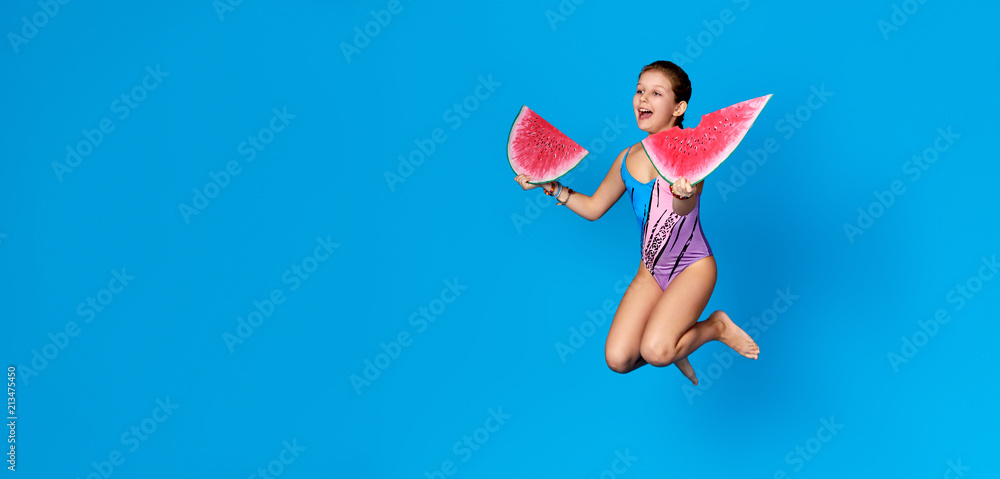 Young girl active jumping up, Studio isolated blue background.Summer concept.Cheerful energy child holding piece of watermelon.Banner,copy space for text,shop,advertising.Kid enjoys vacations,resort.
