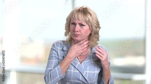 Coughing mature businesswoman. Bright blurred windows in office background. photo