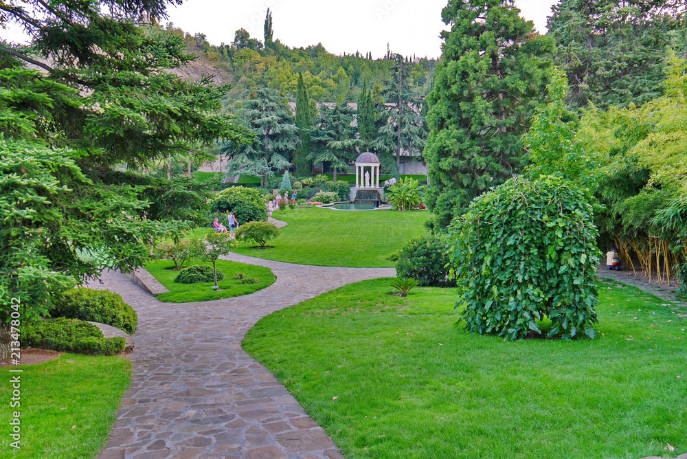 Obraz premium A beautiful view of the green lawns in the park with the paths running between them and people resting on the benches.