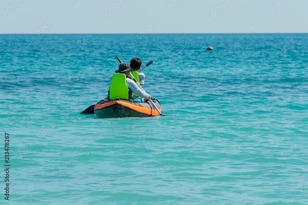 Two male tourists wearing green life jackets, helping Paddle with rubber boats, are in the clear, clean sea water at Koh Samet, a popular tourist destination in Thailand.