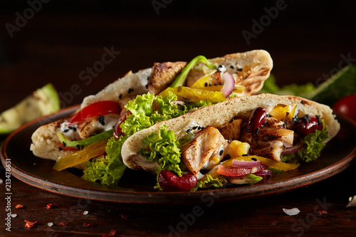 Pita stuffed with chicken, beans and letucce on clay plate over wooden background, side view, selective focus. photo