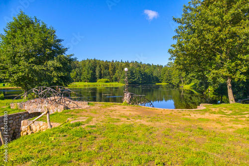 A small footbridge made of stone with a metal forged railing leading to the lake with clear water photo