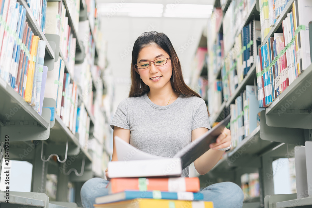 Asian Woman reading and sitting near a bookshelf in the library.. Asian Woman reading and sitting near a bookshelf in the library..