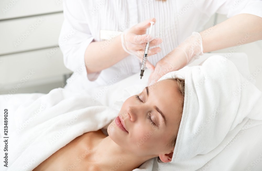 Portrait of pleased girl lying on bed during cosmetic procedure. She getting injection in check Portrait of pleased girl lying on bed during cosmetic procedure. She getting injection in check