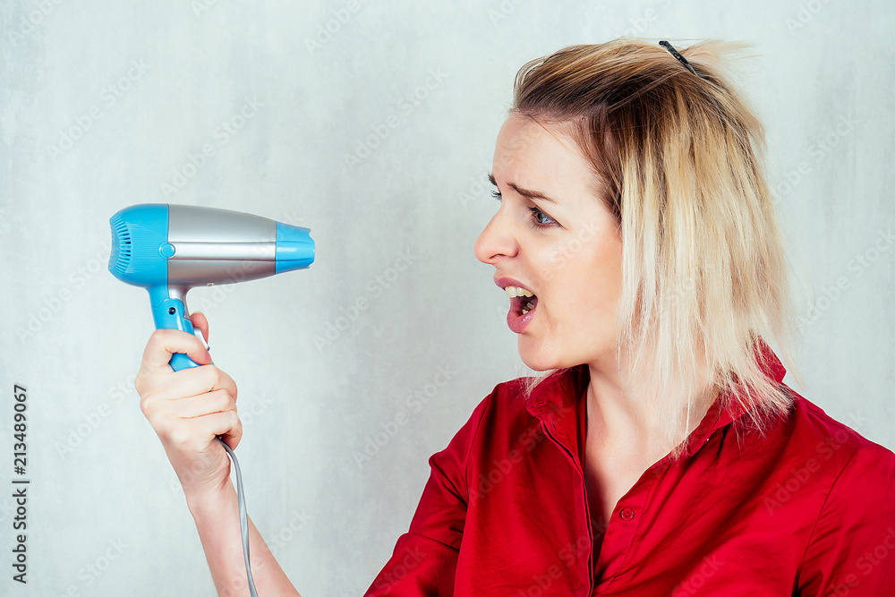 white European woman in white shirt holds blue hairdryer on white background white European woman in white shirt holds blue hairdryer on white background