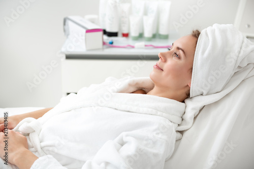 Side view beaming female waiting for treatment procedure while locating on bed in cosmetology clinic