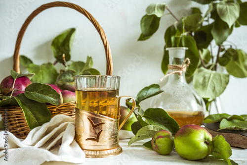 Apple tea in a glass goblet and a decanter and a basket with ripe apples on a wooden table in vintage style