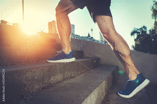 Sport hard. Close up of male feet climbing stairs outside. Well shaped man is jogging at dawn photo