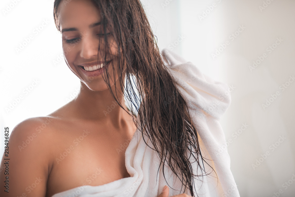 Beaming girl standing in bathroom after taking bath. She holding head with hands Beaming girl standing in bathroom after taking bath. She holding head with hands