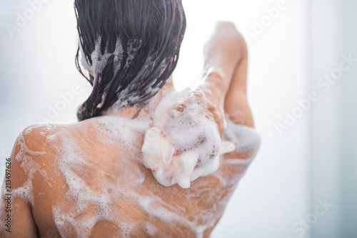 Young lady with smooth skin taking shower with flavorous gel while turning back to camera photo