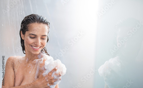Tableau sur Toile Portrait of beaming woman rubbing body with foam while standing under steam of water