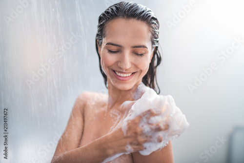Portrait of happy girl taking shower with gel. She washing with puff photo