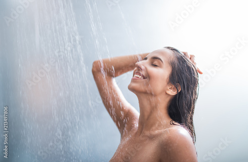 Side view happy woman washes body and hair under stream of hot water photo