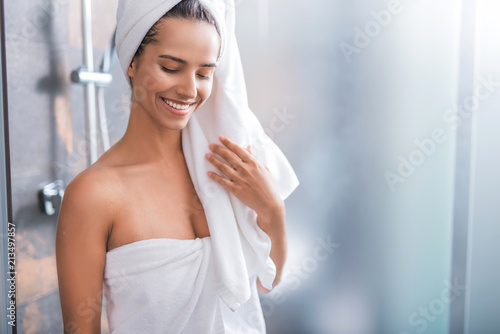 Portrait of cheerful woman wrapping in towel after taking bath. She closing eyes