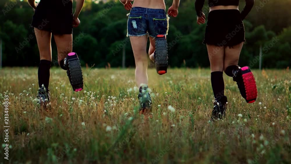 Three girls in boots with springs running through the summer Park at sunset doing sports Three girls in boots with springs running through the summer Park at sunset doing sports