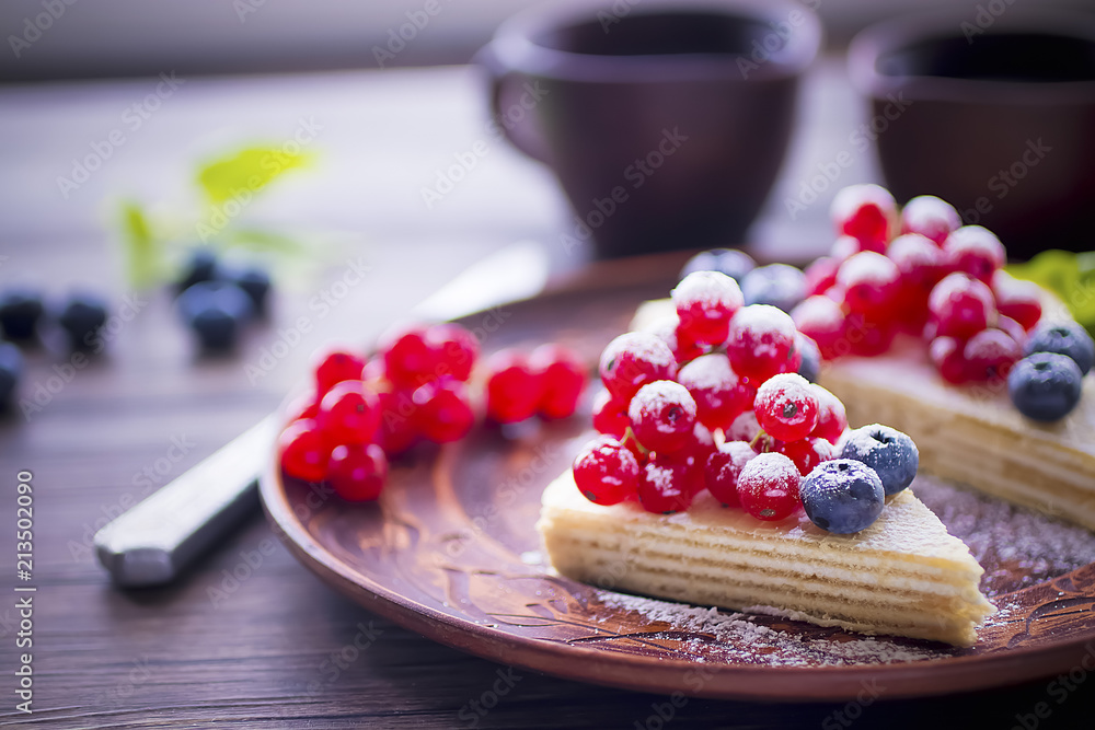 Two pieces of puff cake with fresh berries and sugar powder on brown plate and two brown cups of coffee on dark wooden table. Two pieces of puff cake with fresh berries and sugar powder on brown plate and two brown cups of coffee on dark wooden table.