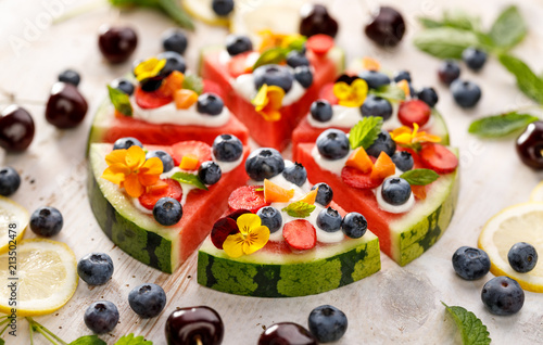 Watermelon pizza with addition of fersh blueberries, strawberries, natural yogurt and edible flowers, Delicious and healthy summer dessert