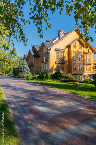 A beautiful summer day landscape in a park with a green lawn and a nearby path and a magnificent house of graceful architecture with a sheathed tree.