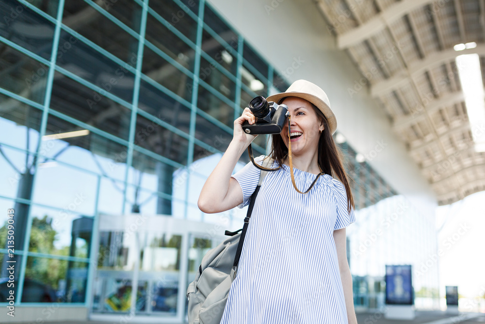 Young traveler tourist woman with backpack taking pictures on retro vintage photo camera at international airport. Female passenger traveling abroad to travel on weekends getaway. Air flight concept.