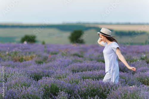 Portrait of young smiling beautiful woman in blue dress, hat on purple lavender flower blossom meadow field outdoors on summer nature, Provence. Happy female run at flowering bush. Lifestyle concept.