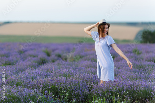 Fototapeta Naklejka Na Ścianę i Meble -  Portrait of young smiling beautiful woman in blue dress, hat on purple lavender flower blossom meadow field outdoors on summer nature, Provence. Happy female run at flowering bush. Lifestyle concept.