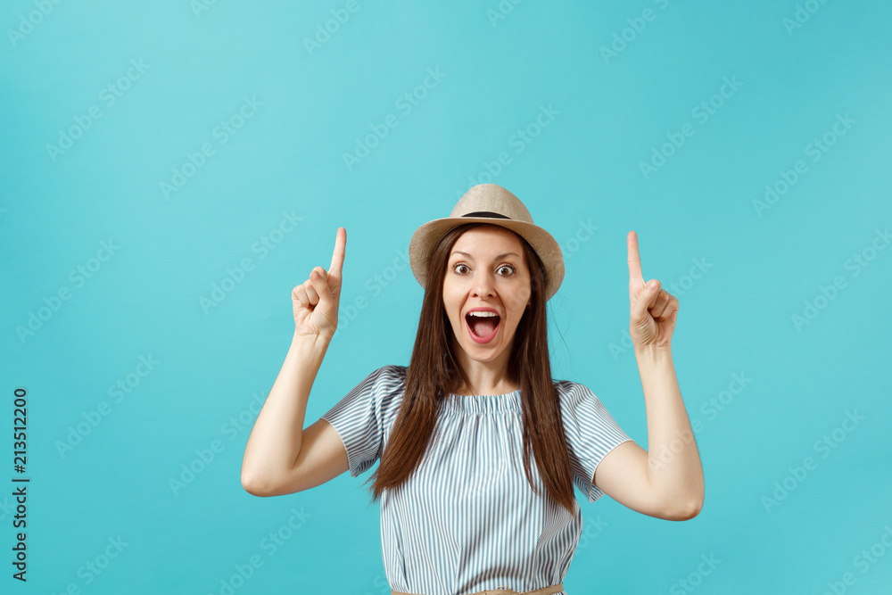 Portrait of excited young elegant woman wearing dress, straw summer hat pointing index fingers up on copy space isolated on blue background. People sincere emotions lifestyle concept. Advertising area Portrait of excited young elegant woman wearing dress, straw summer hat pointing index fingers up on copy space isolated on blue background. People sincere emotions lifestyle concept. Advertising area
