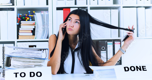 Young secretary talking on the phone forgets about a lot of paper work, which is not done. Inefficient use of working time