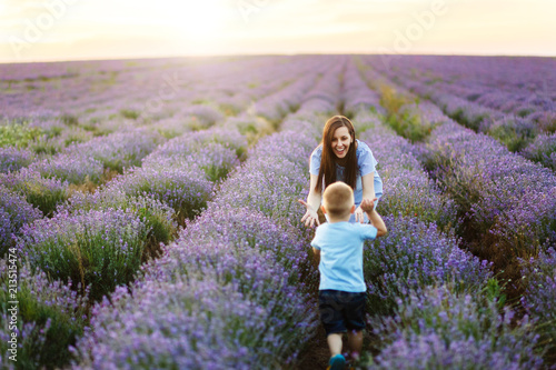 Fototapeta Naklejka Na Ścianę i Meble -  Young woman in blue dress walk on purple lavender flower meadow field background, catch up, have fun, play with little cute child baby boy. Mother, small kid son. Family day, parents, children concept