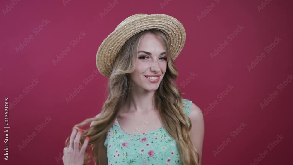 Beautiful young woman in a flowered dress and cute hat turns to camera, happily smiles, seductively plays with her hair, spins around on a colored pink background. Having fun, feeling good, positive Beautiful young woman in a flowered dress and cute hat turns to camera, happily smiles, seductively plays with her hair, spins around on a colored pink background. Having fun, feeling good, positive