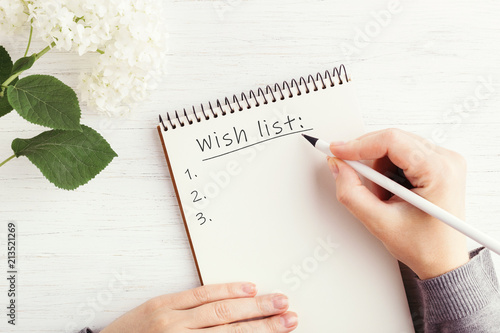Φωτογραφία Woman's hand writing Wish list in notebook on white wooden table