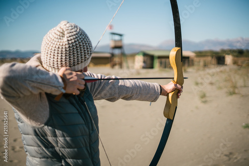 Young female shooting target with her bow and arrow on a sunny day on the beach.