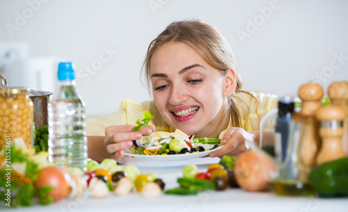 Cheerful girl decorating fresh salad with herbs