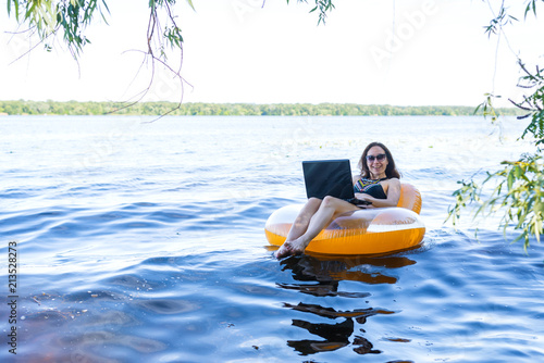 Business woman working on a laptop in an inflatable ring on the river, the concept of working on vacation.