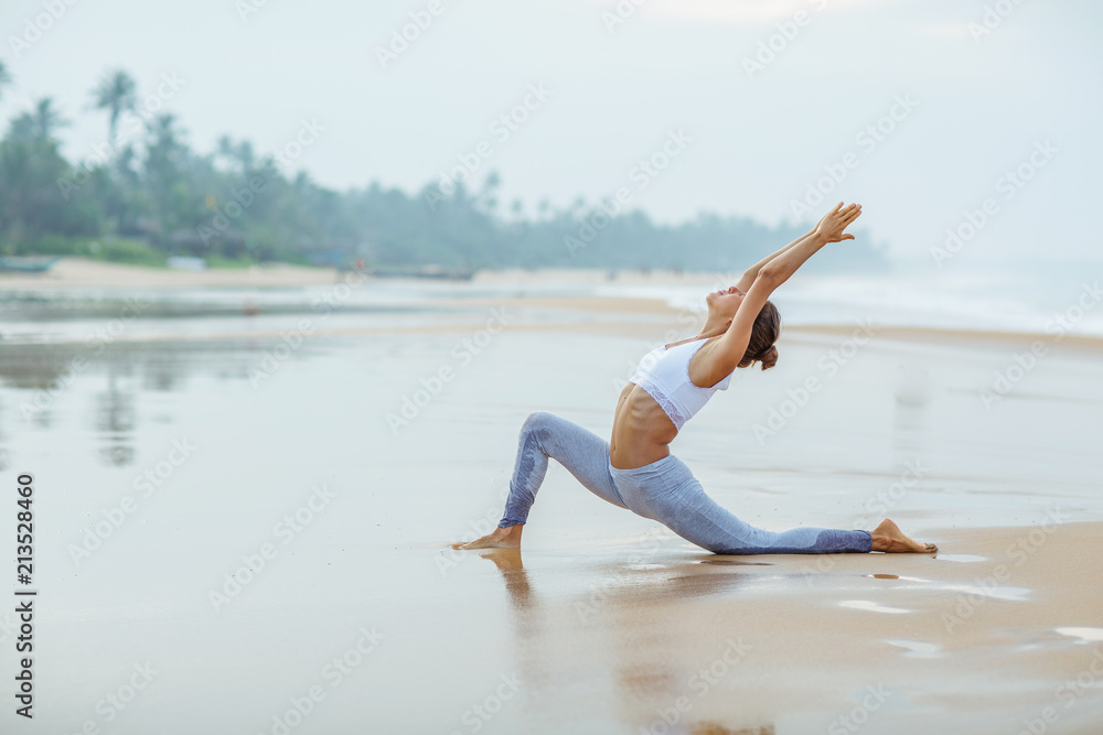 Fototapeta premium Caucasian woman practicing yoga at seashore of tropic ocean