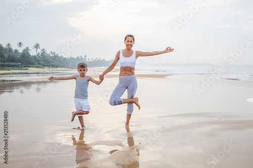 A mother and a son are doing yoga exercises at the seashore of tropic ocean