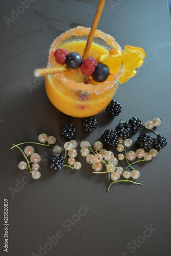 One glass with orange juice fruit, currant, blackberry, orange, gooseberry, straws, sahor on a brown matte background photo