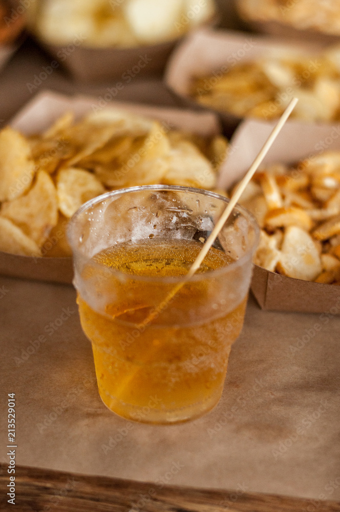 Cool drink of cider, beer, lemonade, in a plastic glass against the background of snacks. close-up, space for text Cool drink of cider, beer, lemonade, in a plastic glass against the background of snacks. close-up, space for text