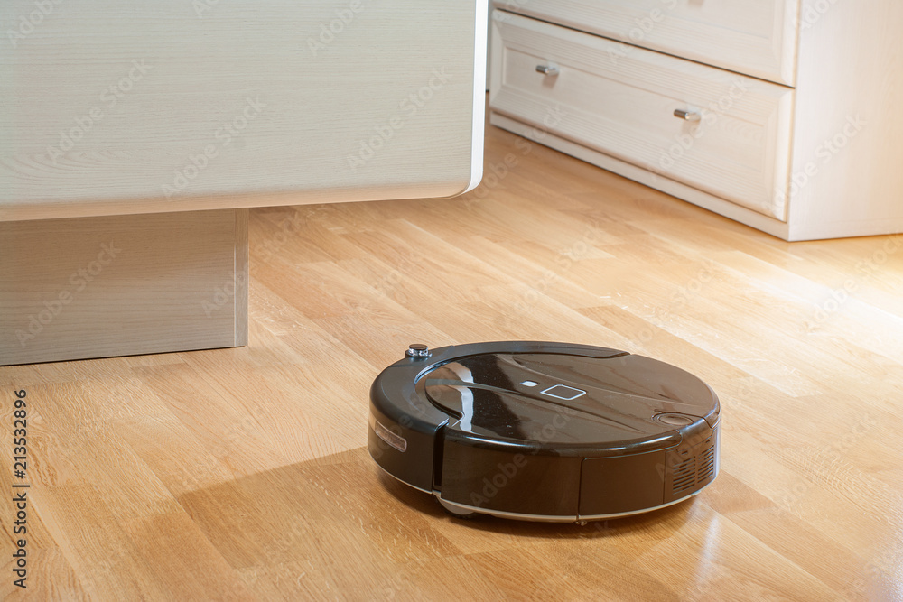 Robot vacuum cleaner runs under bed in bedroom in the rays of the morning sun Robot vacuum cleaner runs under bed in bedroom in the rays of the morning sun