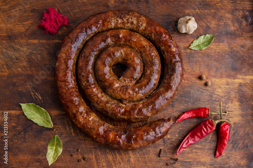Spiral sausage ring baked in an old oven is on a wooden board with pepper and garlic