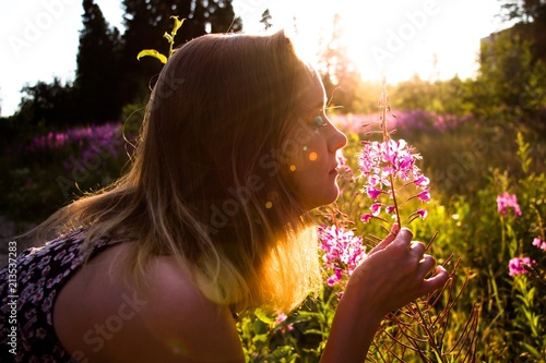 On a sunny meadow among the flowers, on a beautiful sunny, summer and warm day, the girl gets a light touch from the smell of flowers. A light touch keeps the flower and breathes in its delicate fragr photo