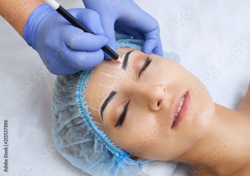 Permanent make-up for eyebrows of beautiful woman with thick brows in beauty salon.  beautician doing  tattooing eyebrow.