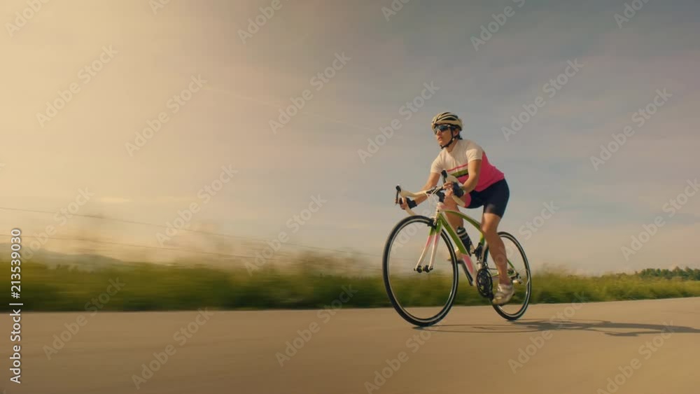 Low wide MS tracking shot of a female cyclist on the road Low wide MS tracking shot of a female cyclist on the road